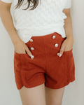 Women's clay-colored high-waisted corduroy shorts with a scalloped edge hemline and decorative button accents on the front.