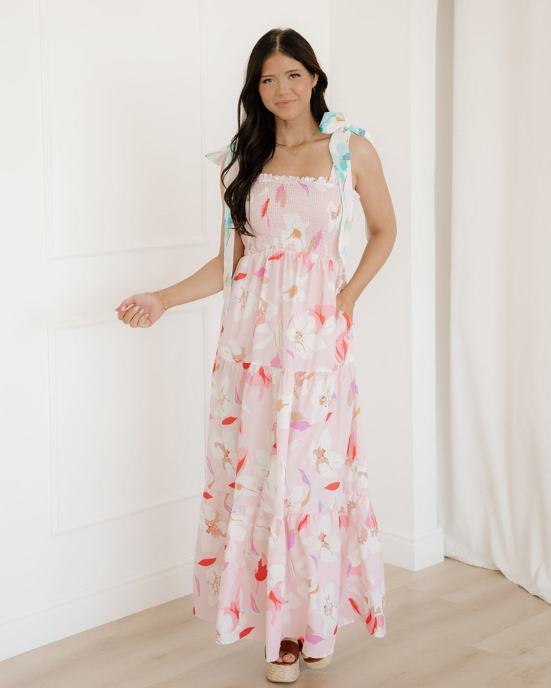 Women's pink floral print maxi dress featuring a smocked bodice, unique knotted tie shoulder straps, and a flowy tiered romantic skirt.
