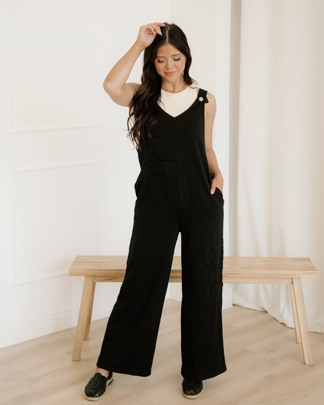Women's loose-fit black utility jumper featuring raw seam detailing, functional pockets, and a large artistic flower patch accent on the leg.