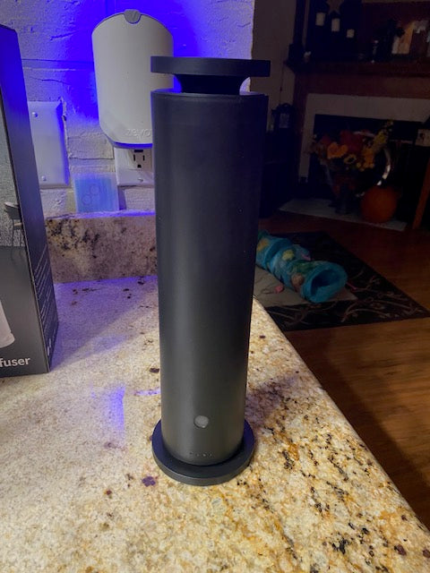 Front view of the sleek, black cylindrical scent diffuser sitting on a dark surface.