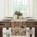 Rustic dining table setup with a beige table runner patterned with black ravens, pumpkins, and crescent moons.
