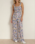 A woman wearing a sleeveless purple boho floral high-waist jumpsuit featuring a square neckline and a comfortable stretch bodice.