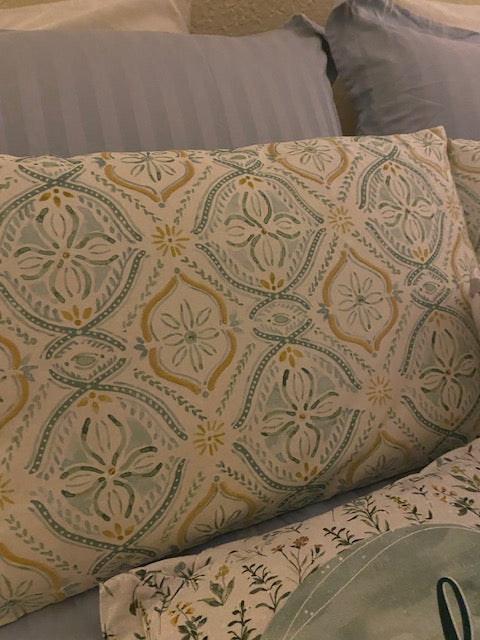 Square accent pillow featuring an intricate olive and gold vintage damask and medallion pattern, displayed on a bed alongside a solid green pillow