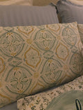 Square accent pillow featuring an intricate olive and gold vintage damask and medallion pattern, displayed on a bed alongside a solid green pillow