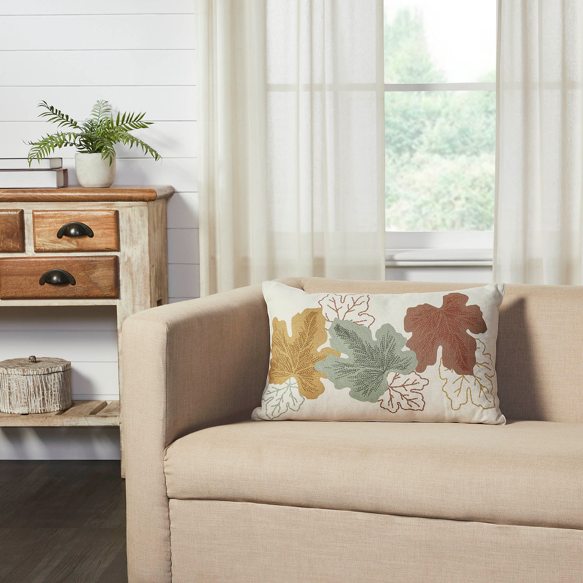 Bountiful Leaves embroidered throw pillow displayed on a neutral beige armchair in a cozy living room setting.