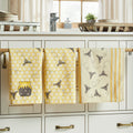 Three kitchen towels with bee and honeycomb patterns hanging on a rack in a kitchen.
