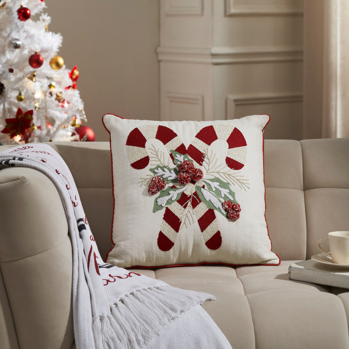 Embroidered Christmas candy cane throw pillow styled on a cream sofa next to a decorated Christmas tree.