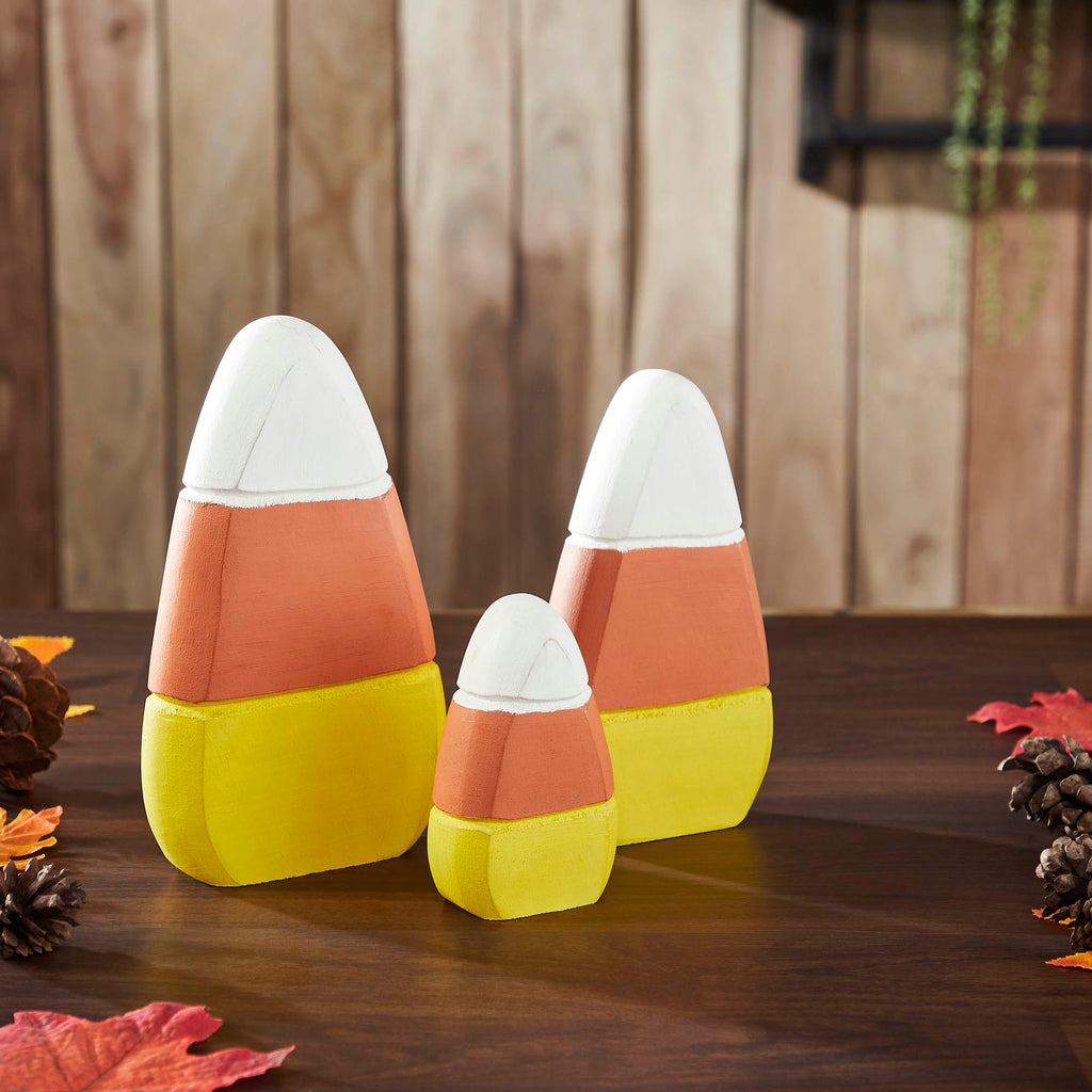 Set of three rustic wooden candy corn decor pieces displayed on a wooden surface with seasonal fall leaves.
