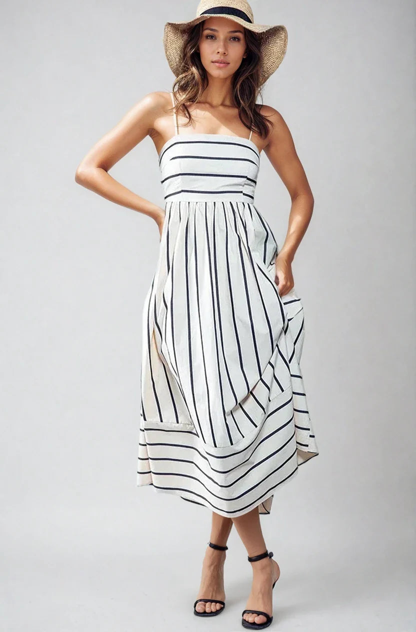 A woman wearing the Salt & Soul navy and white vertically striped midi dress with an open back and adjustable straps, standing in a sunlit outdoor setting.