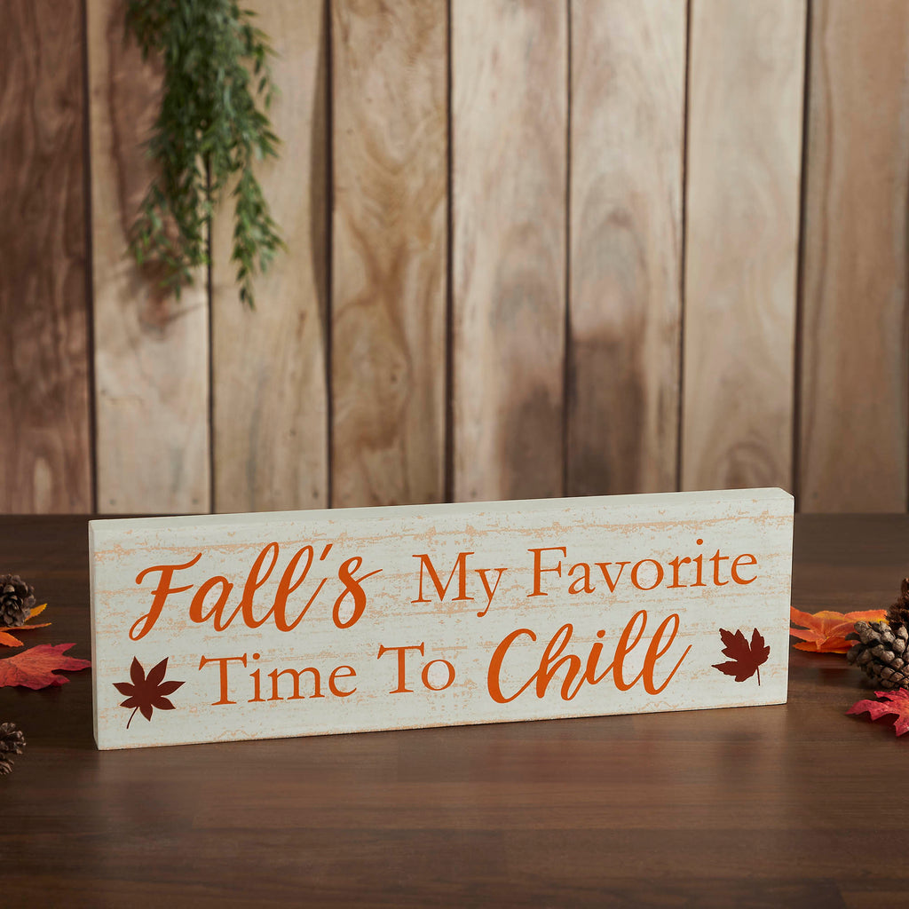 Rustic wooden sign reading "Fall's My Favorite Time To Chill" with orange leaves on a wood plank backdrop.
