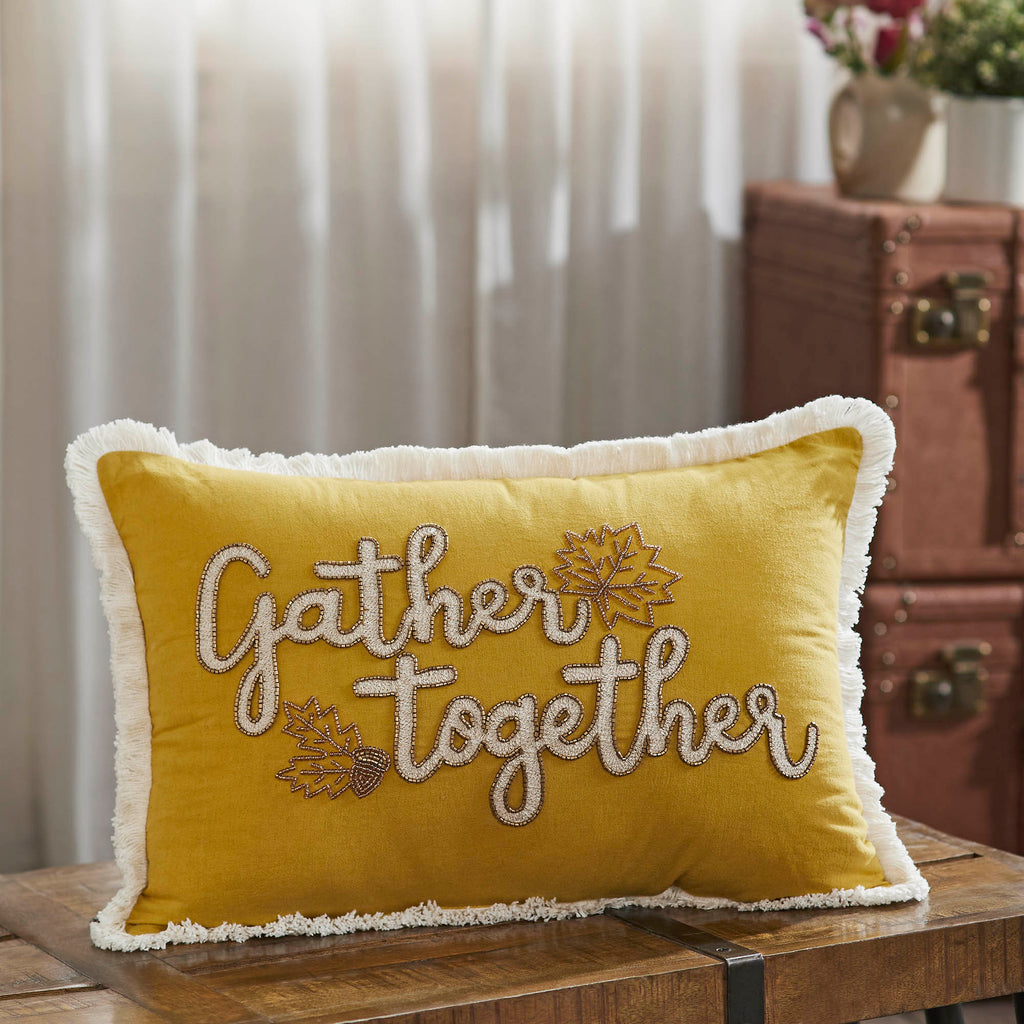 Gather Together embroidered yellow velvet throw pillow displayed on a brown leather bench in a rustic living room.