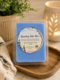 Closer view of Growing Into Her soy wax melts package placed on a wooden surface next to a decorative electric ceramic wax warmer.