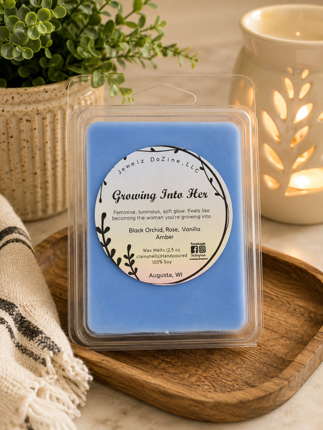 Closer view of Growing Into Her soy wax melts package placed on a wooden surface next to a decorative electric ceramic wax warmer.