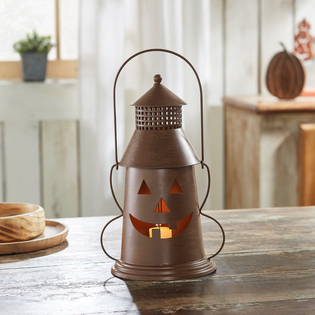 Bronze metal jack-o'-lantern tea light lantern sitting on a wooden dining table next to fall decor.