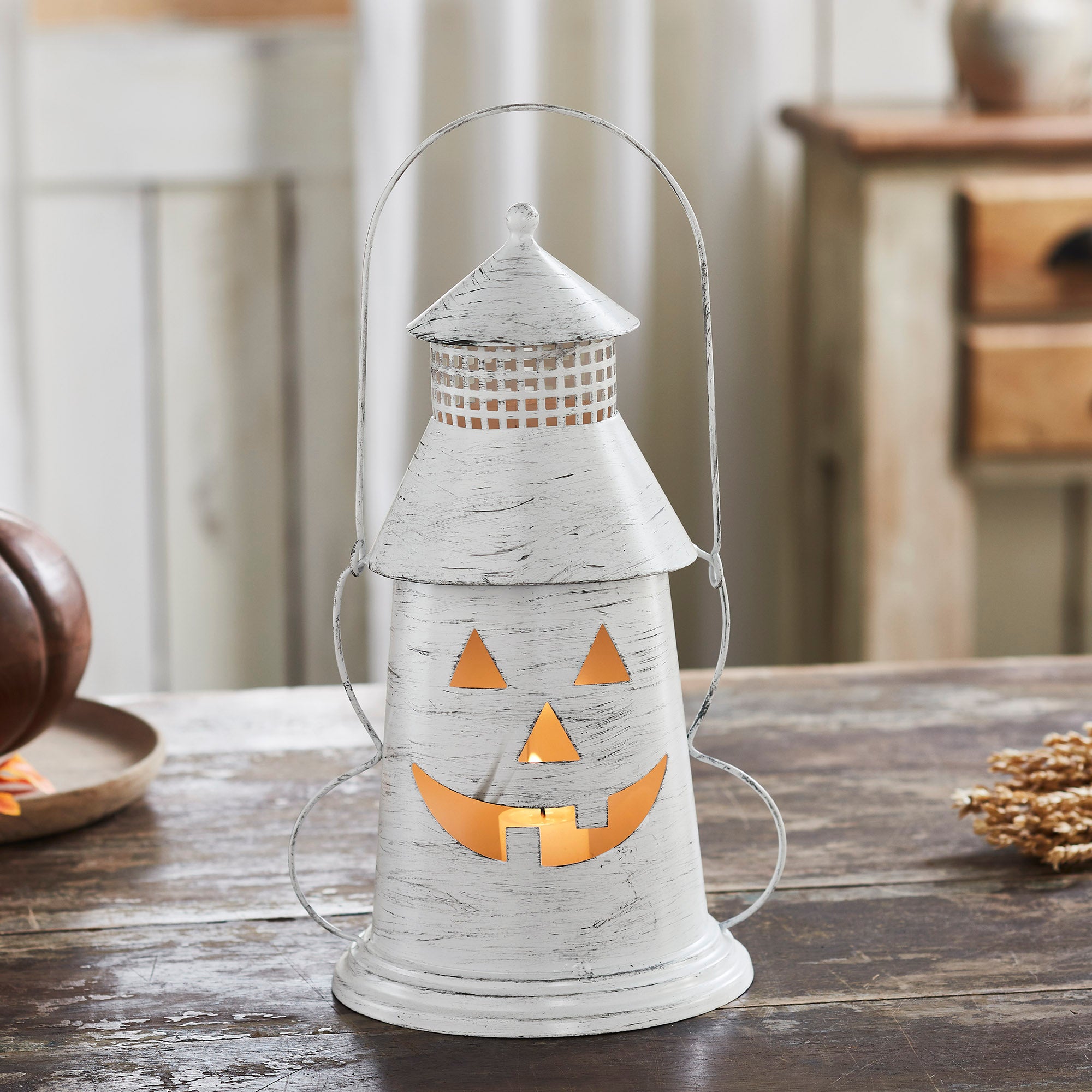 Distressed white metal jack-o'-lantern lantern with tea light burning inside on a rustic table.