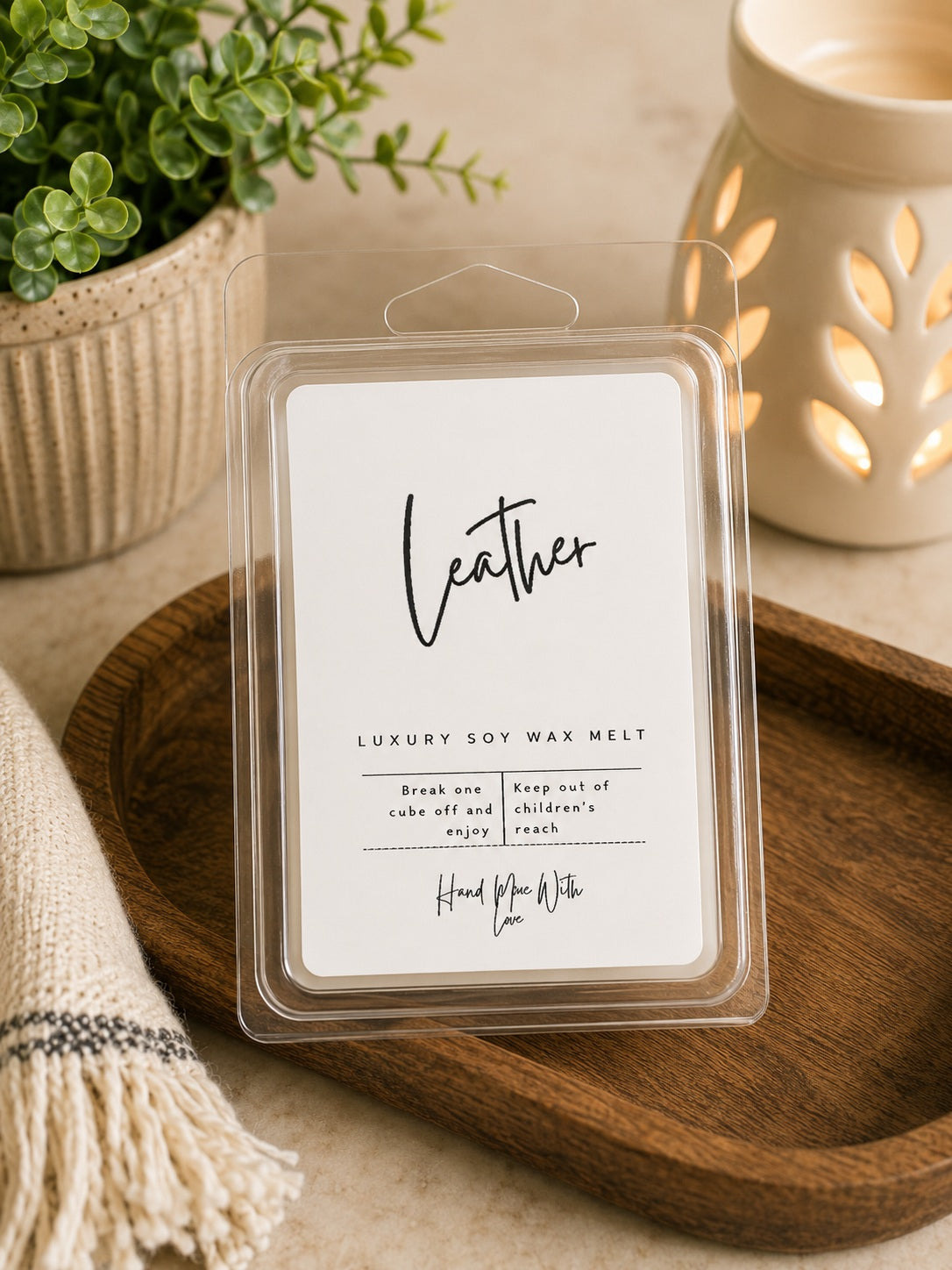 Package of Leather soy wax melts sitting next to a ceramic wax warmer on a rustic surface.