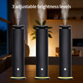 Black cold-air scent diffuser standing upright with light mist vapor rising from the top, demonstrating three adjustable ambient light brightness levels along its base.
