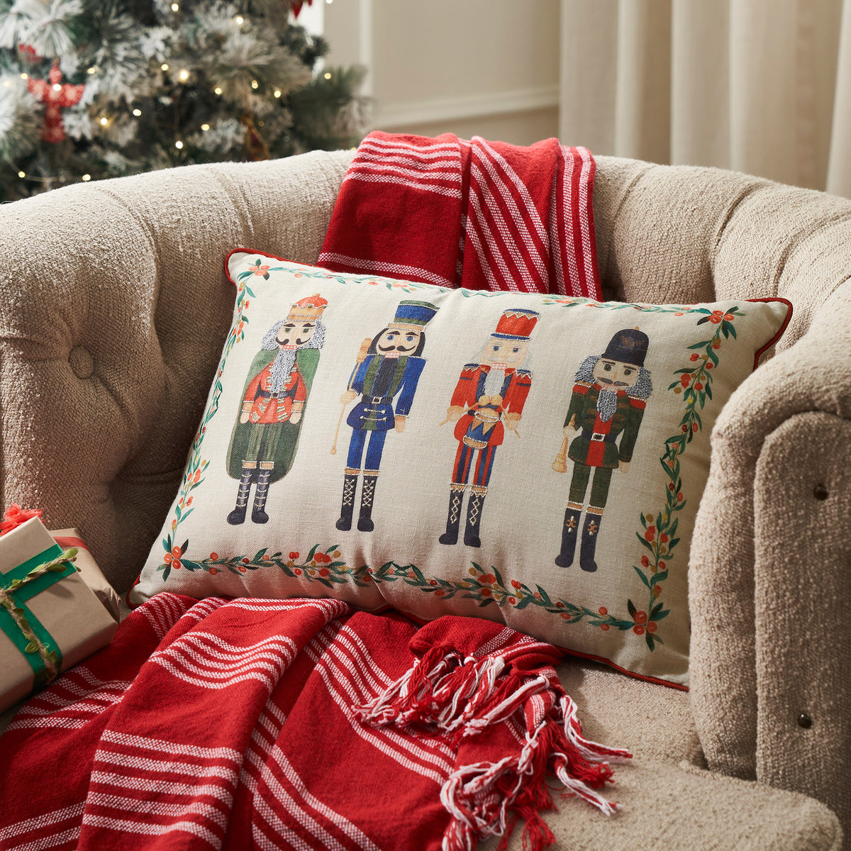 Nutcracker embroidered lumbar accent pillow styled on a living room sofa next to a red plaid throw blanket.