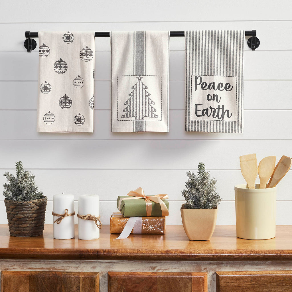 Set of 3 Christmas tea towels featuring "Peace on Earth" text, a Christmas tree print, and holiday accent patterns hanging in a kitchen setting.
