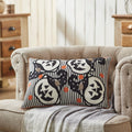 Vintage style Halloween accent pillow with printed jack-o'-lanterns and ticking stripes placed on a neutral armchair in a cozy rustic living room setup.
