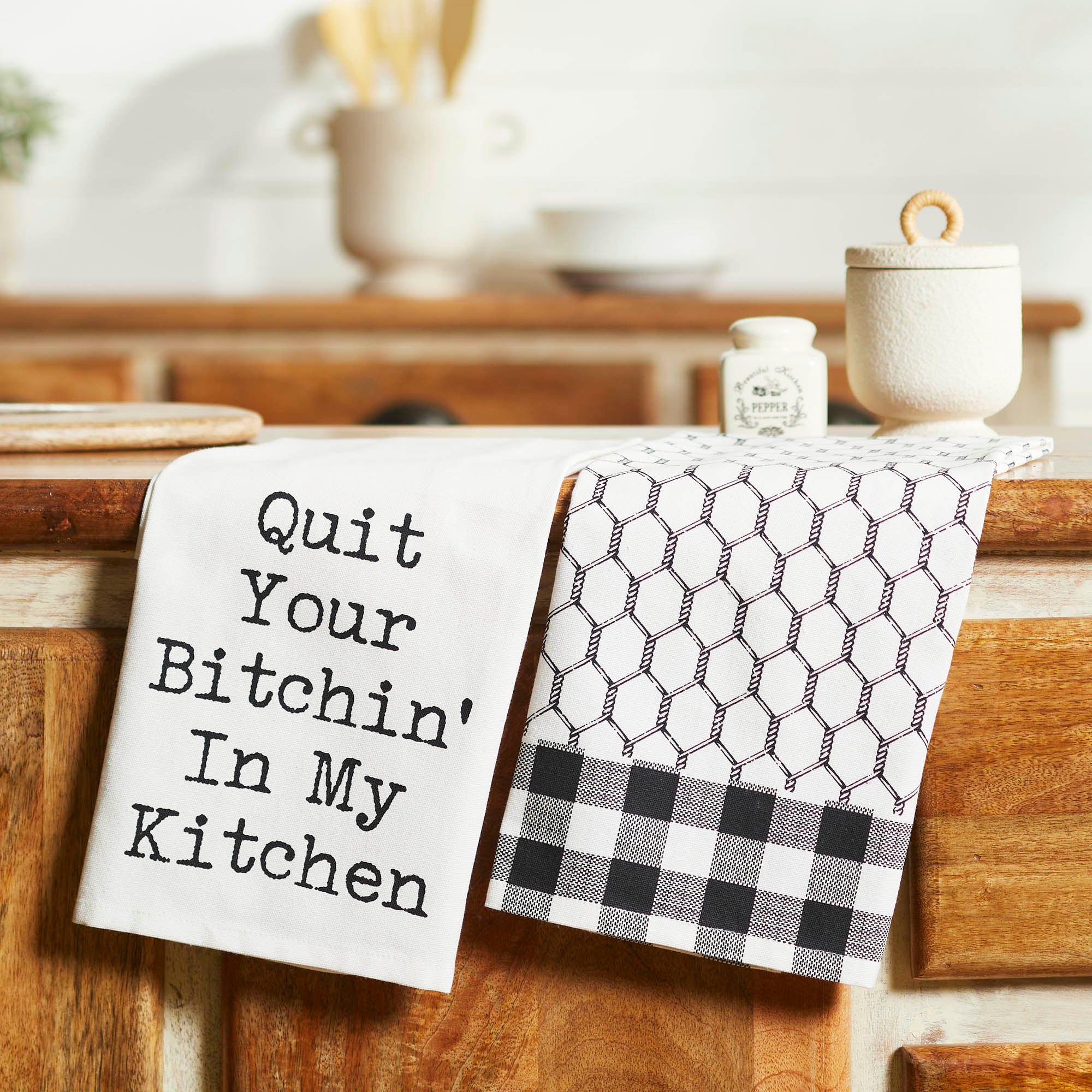 Set of two black and white kitchen towels. One reads "Quit Your Bitchin' In My Kitchen" and the other features a black chicken wire and gingham check pattern.