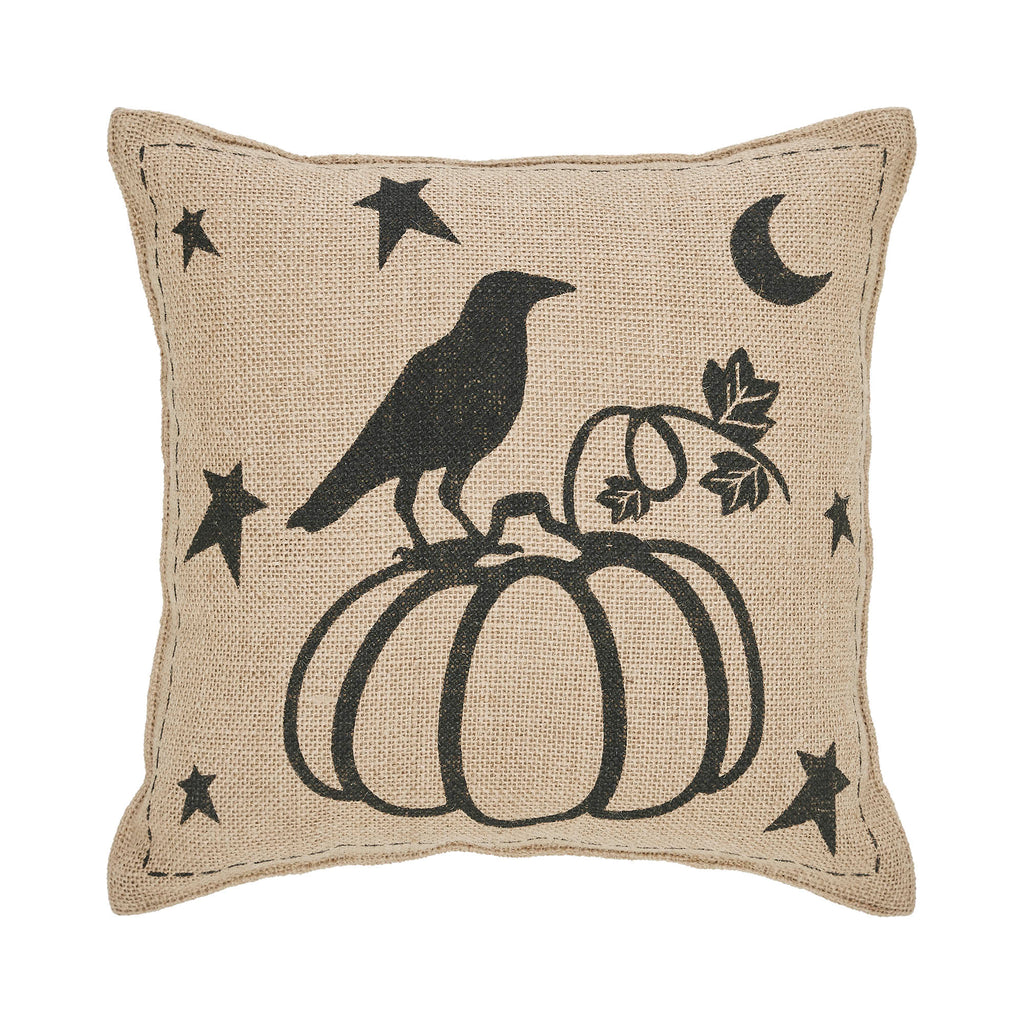 Square throw pillow featuring a black raven perched on a pumpkin with crescent moons and stars on woven fabric.