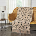 Midnight Harvest woven throw blanket with black ravens, pumpkins, stars and moons draped over a wicker bench in a bright living room.
