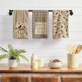 Set of three fall kitchen towels featuring pumpkins, ravens, gingham, grain sack stripes and "Under the Harvest Moon" text displayed on a black wall-mounted towel bar.