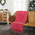 Red and white plaid woven throw blanket draped over a natural wood armchair in a cozy Christmas room setup.
