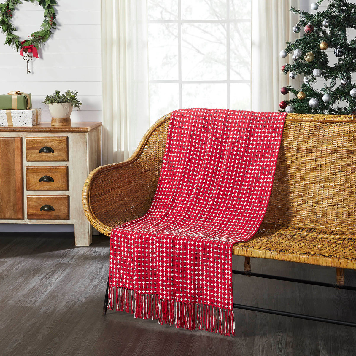 Red and white plaid woven throw blanket draped over a natural wood armchair in a cozy Christmas room setup.