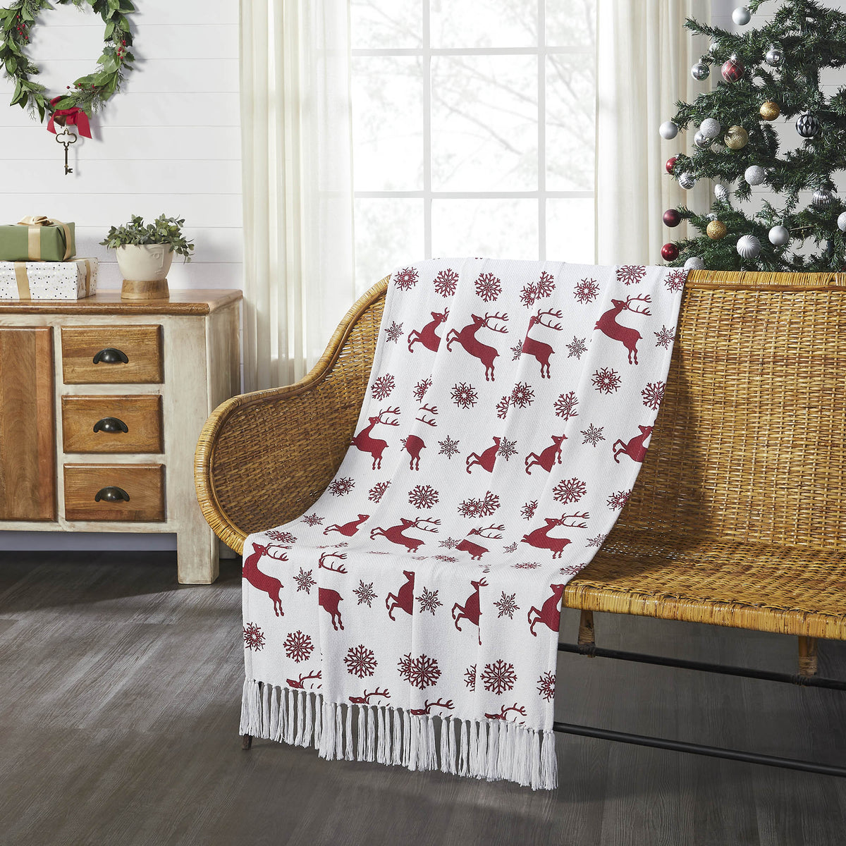 Rustic Christmas woven throw blanket with red reindeer and green tree pattern styled over an armchair near a Christmas tree.