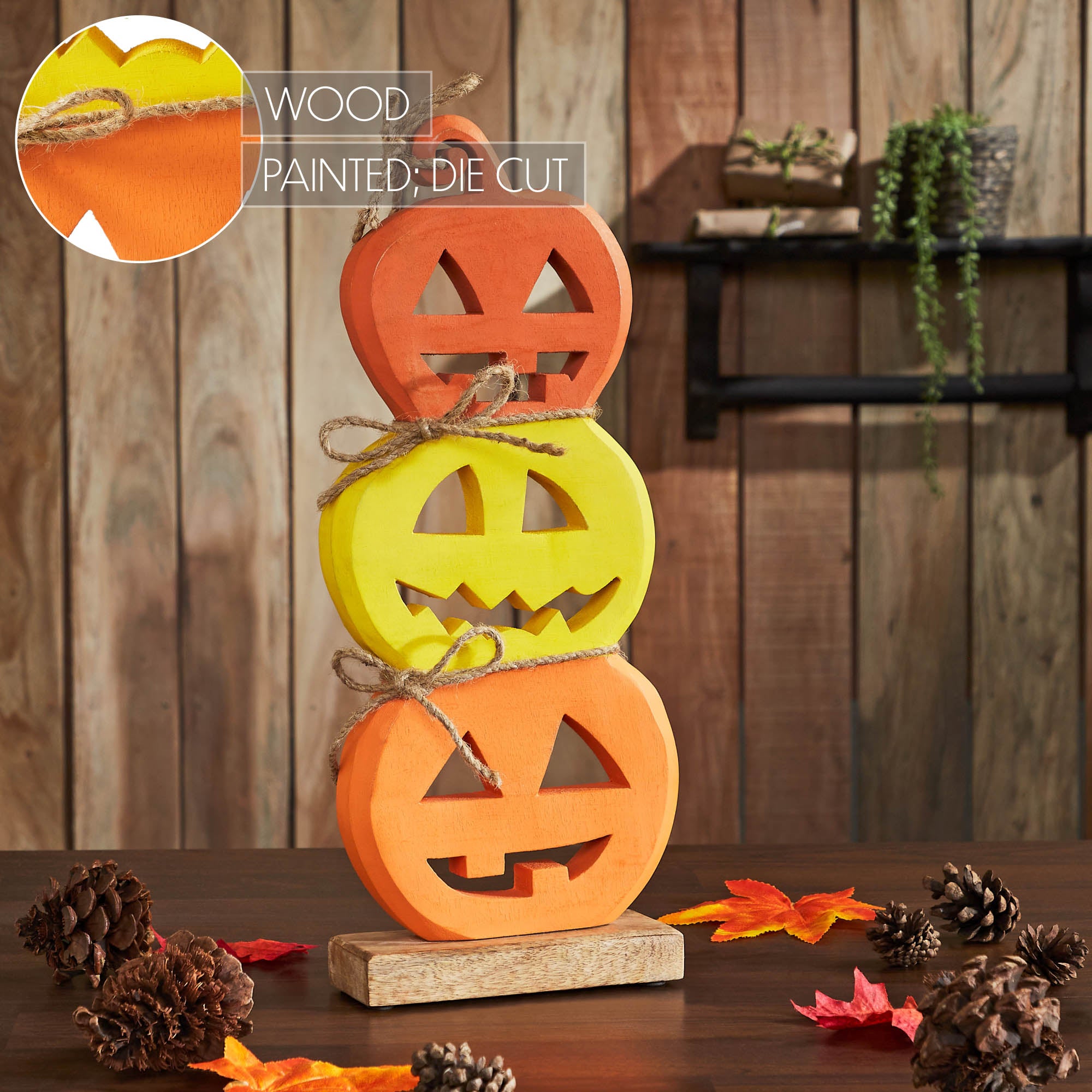 Wooden jack-o'-lantern trio styled indoors on a cozy table setup alongside pinecones and leaf garlands.