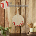 Rustic paddle-shaped wooden cutting board sign with "Thankful" script displayed against a wood plank background.